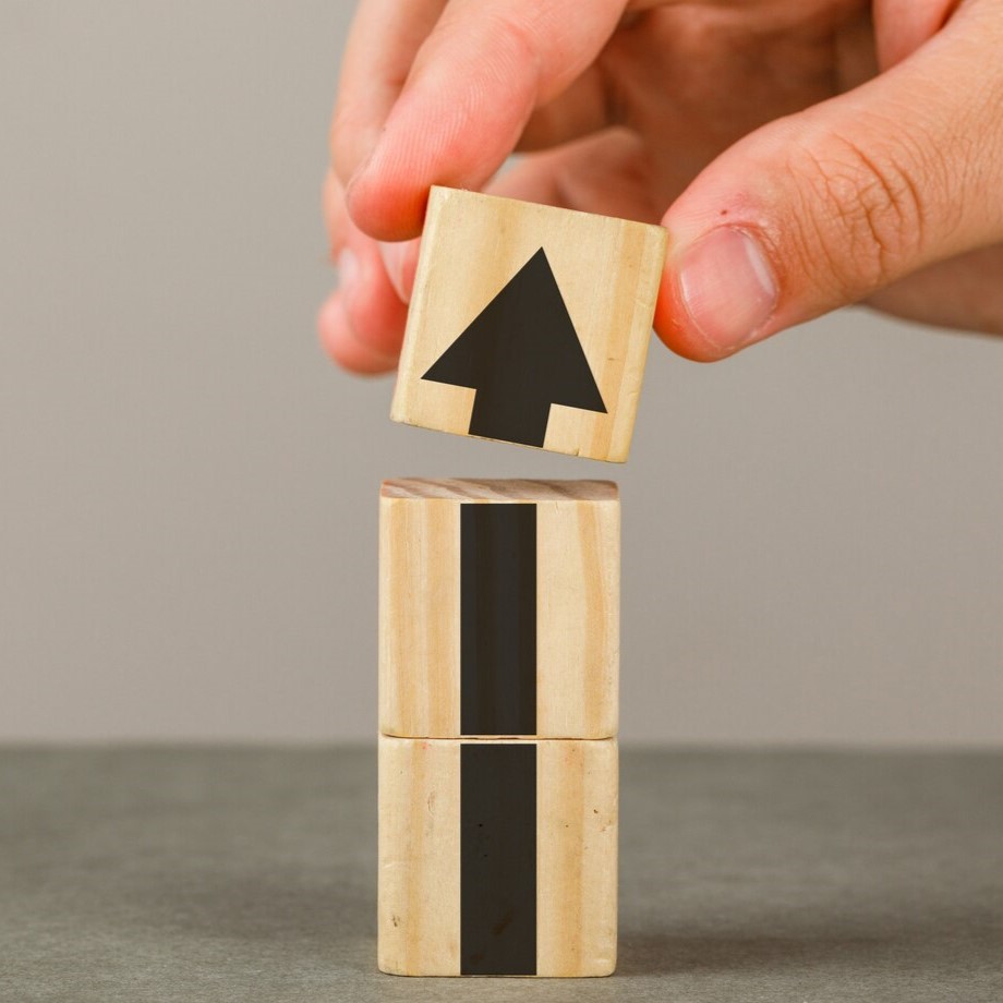 business-growth-concept-grey-white-wall-side-view-hand-putting-wood-block-onto-tower_176474-6577_2